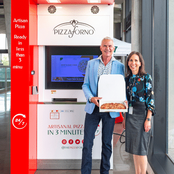 A man and woman showing off a Pizza they received from a Pizzaforno indoor kiosk.