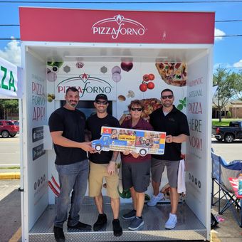 A group standing inside a Pizzaforno outdoor kiosk for a charity event.