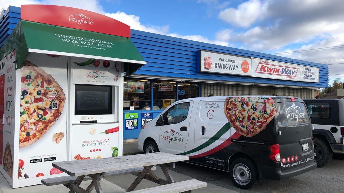 An outdoor pizza vending machine with a PizzaForno van parked beside it. The PizzaForno outdoor kiosk has a picnic table in front of it.
