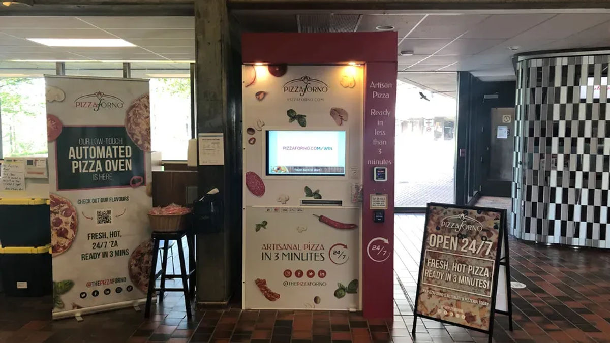 A picture inside the University of Toronto Scarborough building that shows a PizzaForno pizza vending machine with promotional signs beside it.