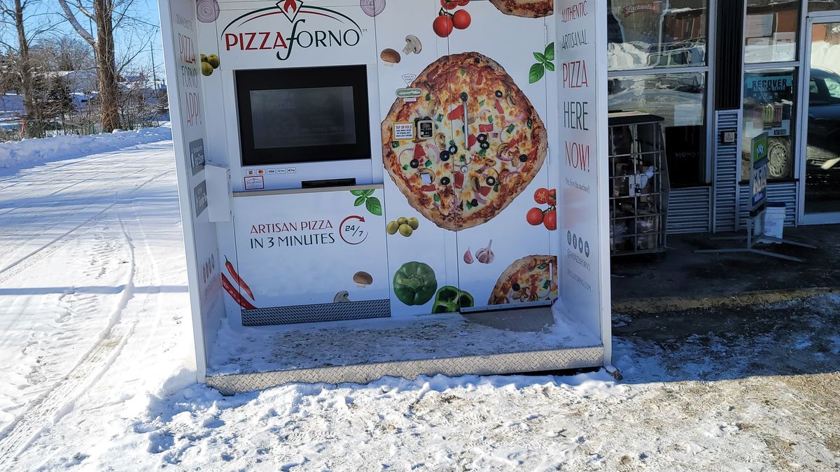 A pizza vending machine that is outside of a store during the winter in Sudbury.
