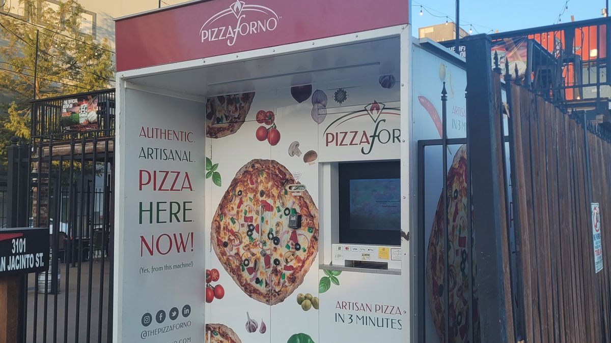 An empty parking lot at the Beer Garden in Houston, Texas that has a PizzaForno machine and an ice maker. The palm tree is behind the pizza vending machine.